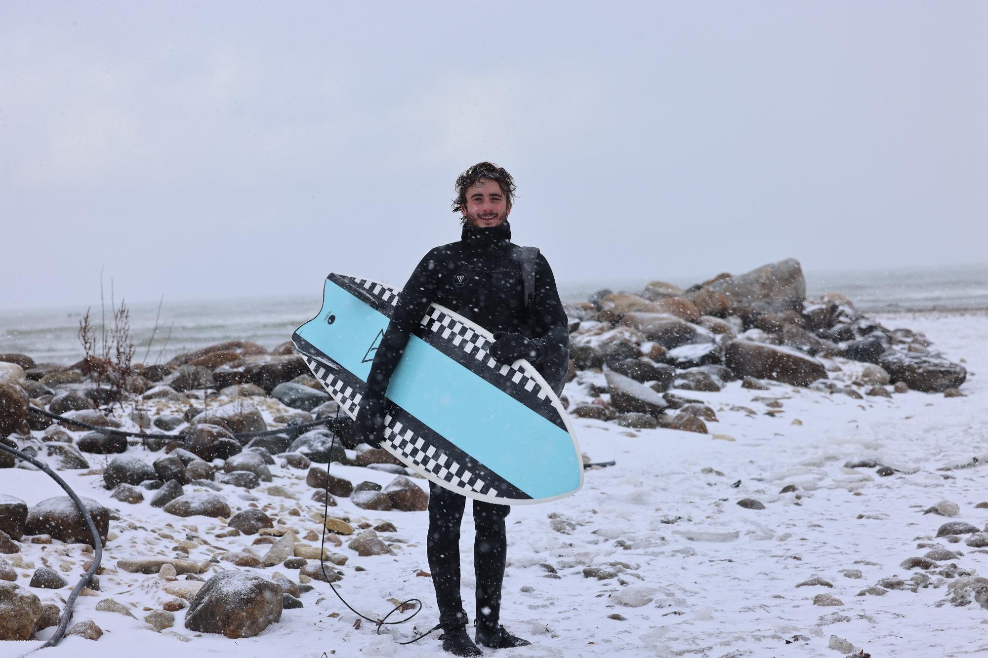 Founder standing with surfboard on a snowy shoreline